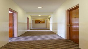 A hotel hallway with carpeted floors, wooden doors, and a painting on the wall. - MeroStay 167 Serenity (Kathmandu)