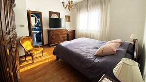 Ein Schlafzimmer mit Bett, Stuhl, Kommode, Fernseher und einer Chandelier.