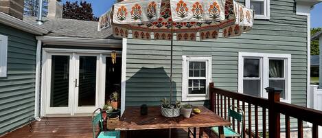 A wooden deck with a table and chairs, a covered patio area with a decorative umbrella, and a house with a green exterior and white trim.