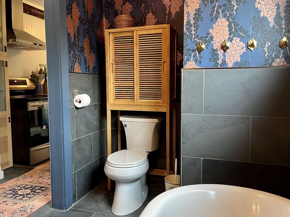 A bathroom with a toilet, a bathtub, and a wooden cabinet above the toilet. - Burnham Cottage (Springfield Center)