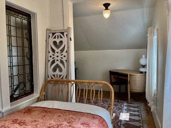 A bedroom with a bed, a window with a decorative screen, a ceiling light, a desk, and a chair.