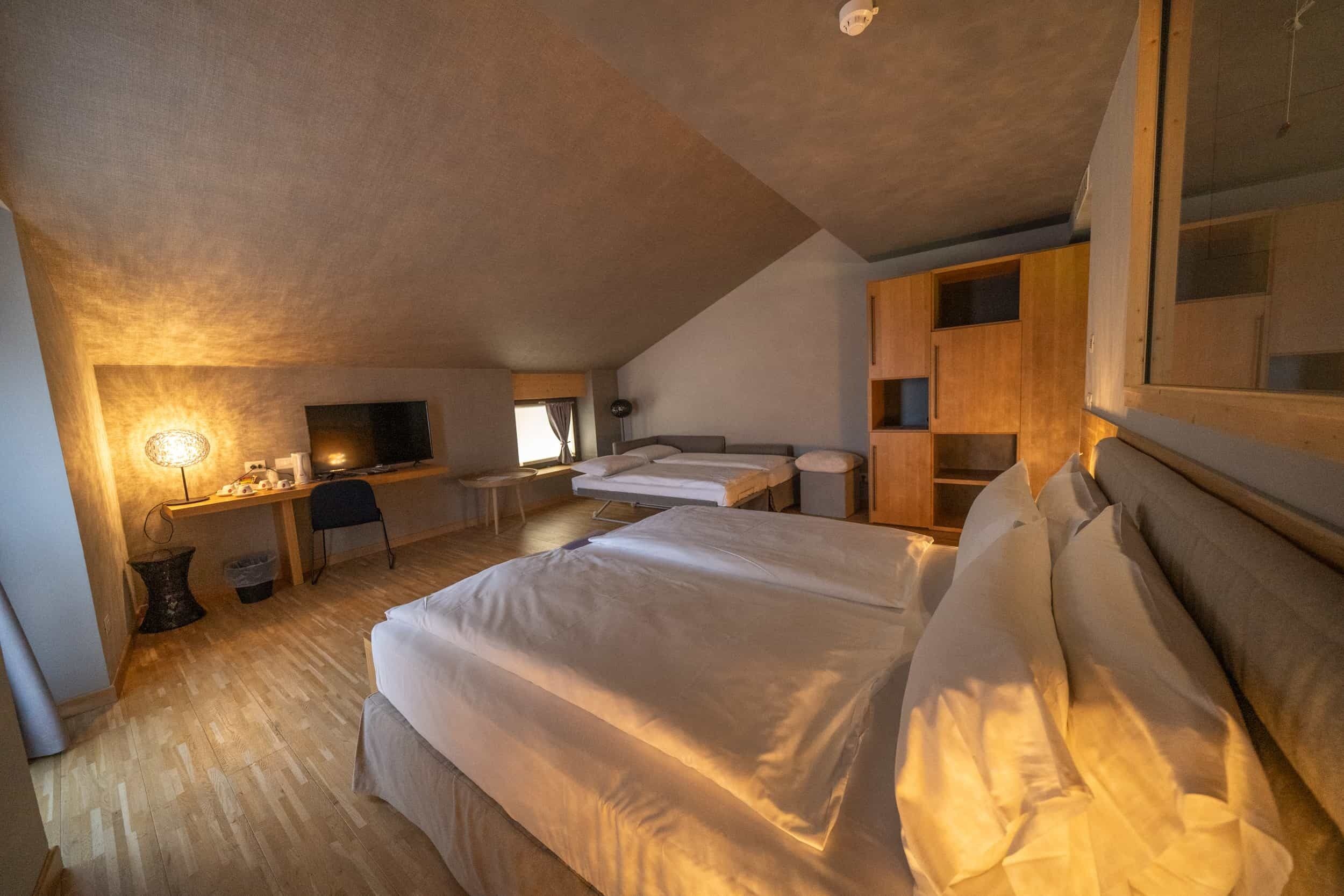 A bedroom with a large bed, a desk, a chair, and a TV.