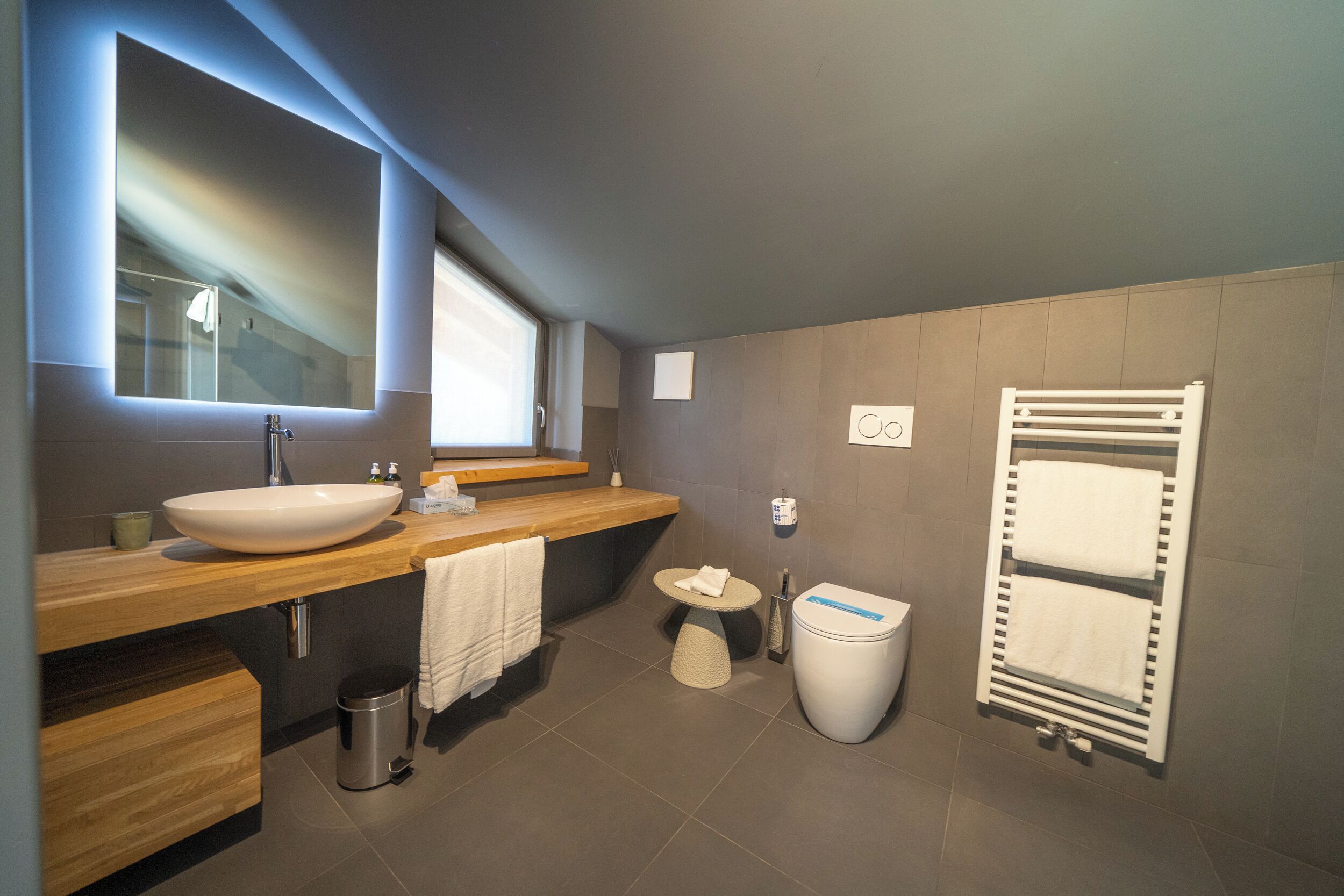 A modern bathroom with a large mirror, wooden vanity, white sink, and a towel rack.