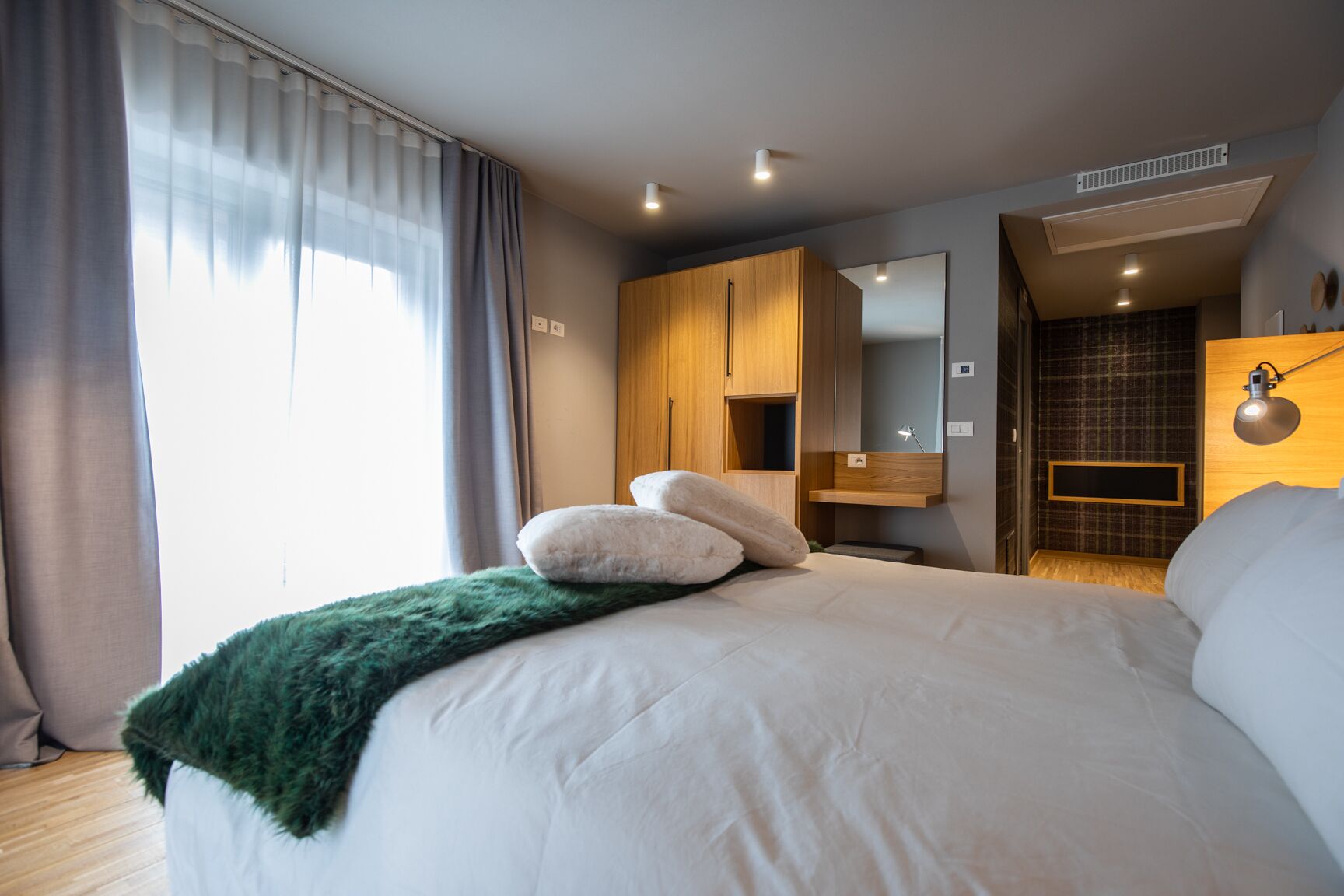 Een moderne slaapkamer met een groot bed, een groene deken en een houten garderobe.
