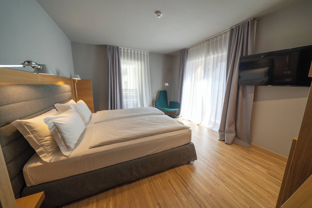 A modern hotel room with a large bed, a flat-screen TV, and a wooden floor.