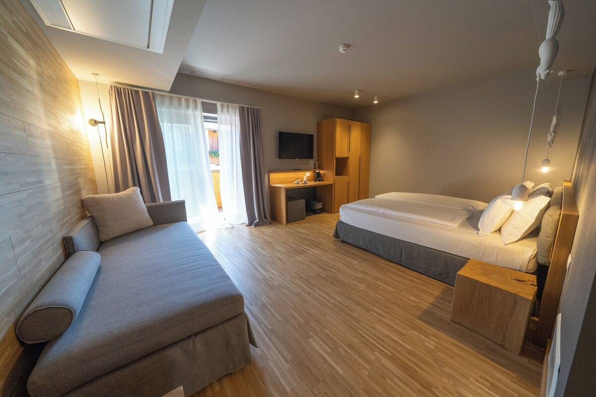 A modern hotel room with a sofa, a bed, a desk, and a TV.