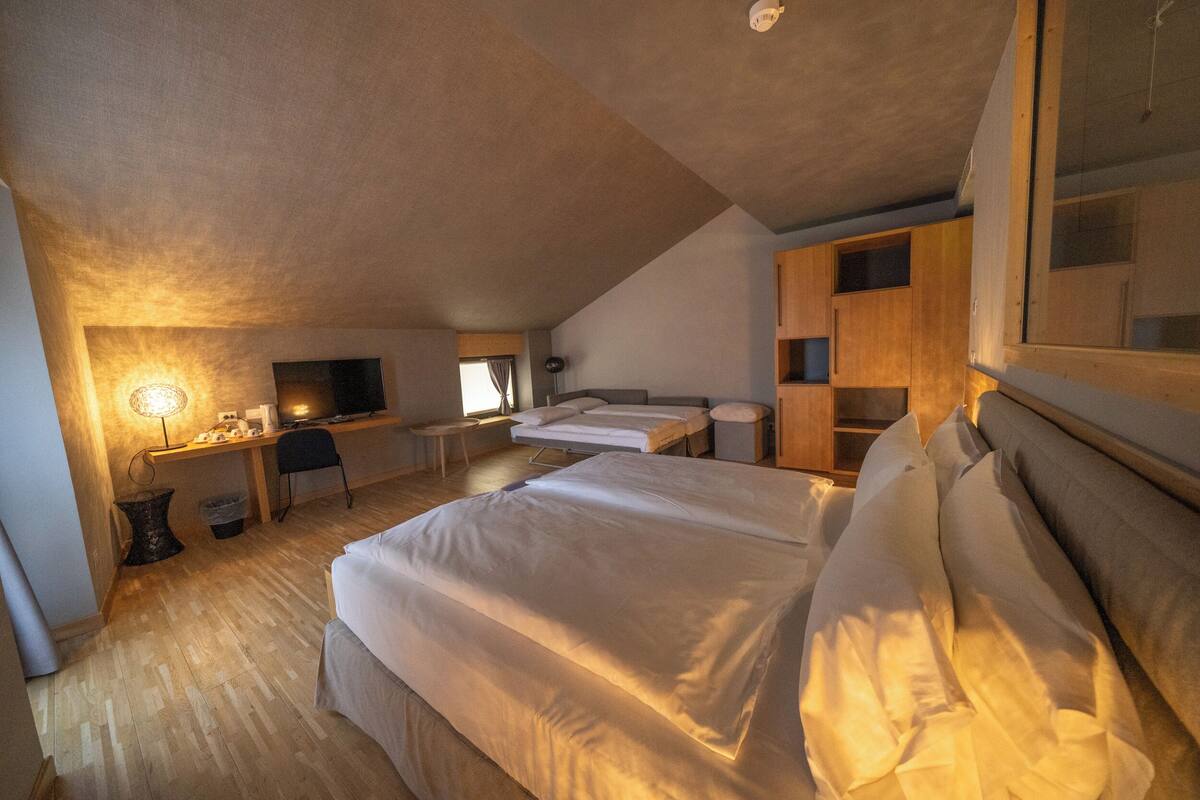A bedroom with a large bed, a desk, a chair, and a TV.