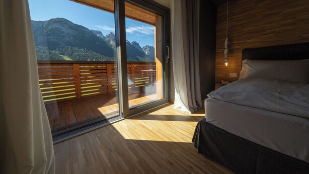 A bedroom with a large sliding glass door leading to a balcony with a mountain view. - Bach Boutique Hotel (Sappada)