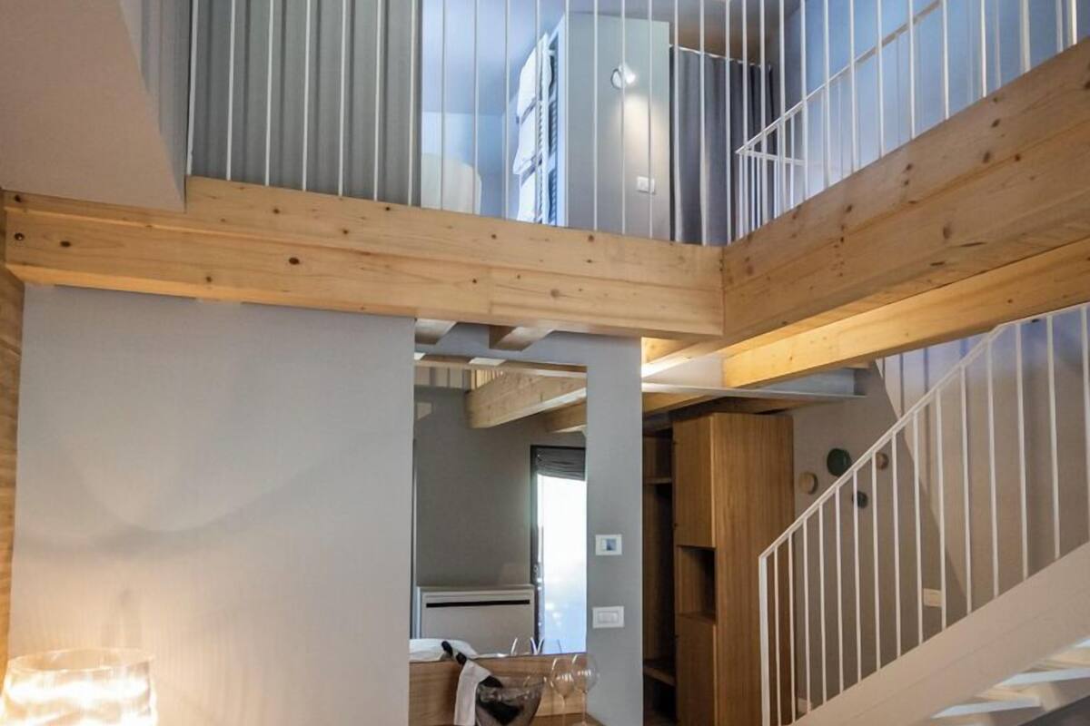 A modern hotel room with a lofted sleeping area, wooden beams, and a staircase.