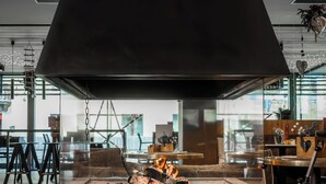 A modern interior with a large fireplace, a stack of firewood, and a view of the city through large windows. - Bach Boutique Hotel (Sappada)