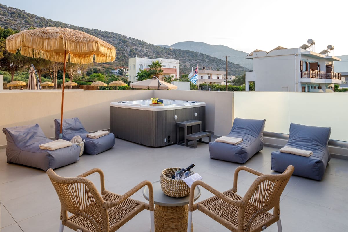 A rooftop terrace with a hot tub, lounge chairs, and a thatched umbrella.