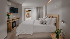 A modern bedroom with a large bed, a TV mounted on the wall, a small desk, and a view of the outdoors.