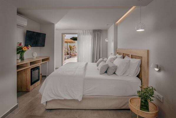 A modern bedroom with a large bed, a TV mounted on the wall, a small desk, and a view of the outdoors.