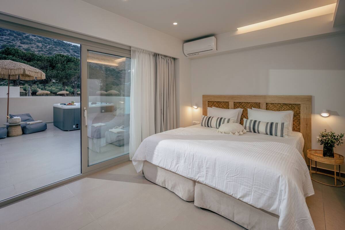 A modern bedroom with a large bed, a glass door leading to an outdoor area, and a view of a mountainous landscape.
