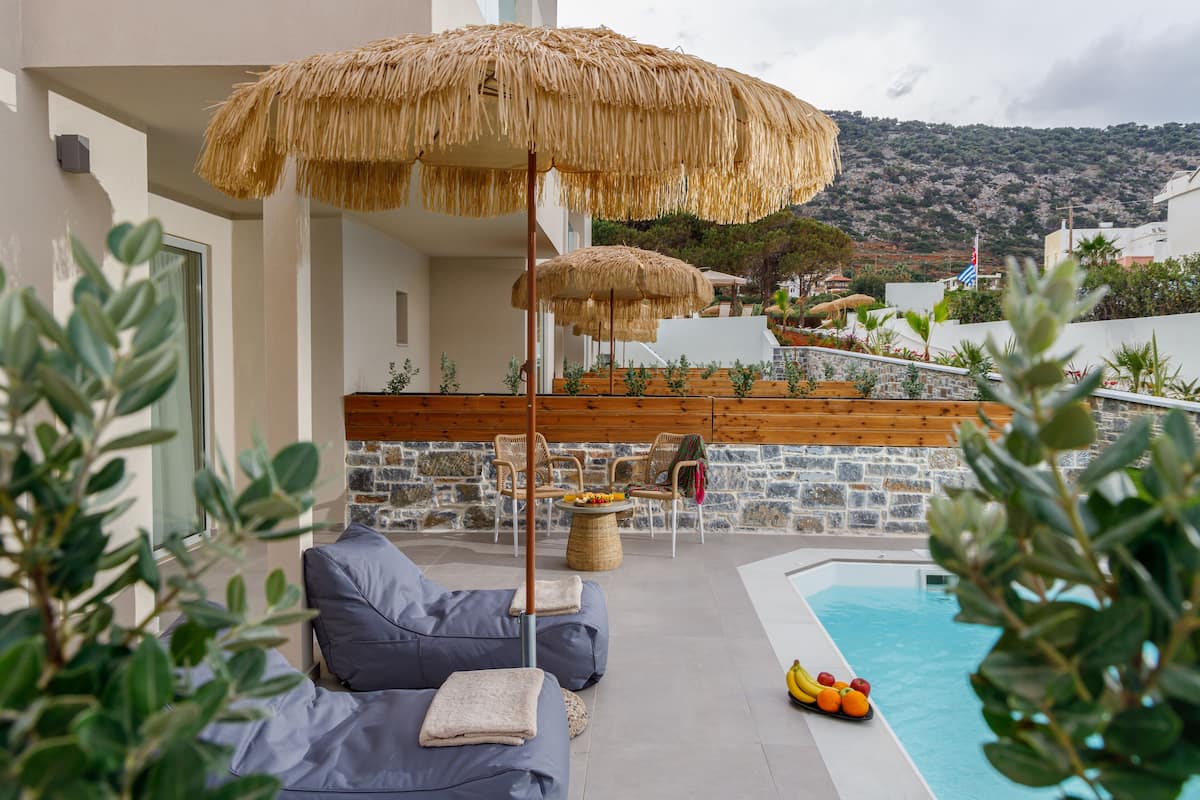 A poolside area with a lounge chair, a table with fruit, and a view of a mountain.