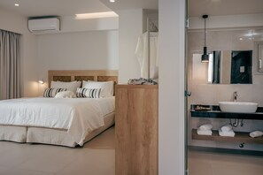 A modern hotel room with a large bed, a wooden headboard, a glass-enclosed bathroom with a sink and towel rack. - Anassa Suites by Estia Adults Only (Hersonissos)
