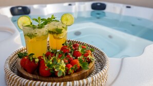 A hot tub with two glasses of a yellow beverage garnished with lime and mint, and a wooden tray with fresh strawberries.