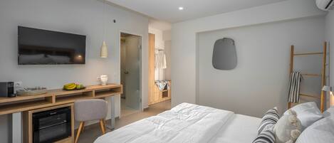 A modern hotel room with a bed, a desk with a computer, a television, and a small kitchenette.