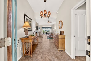 A hallway with a chandelier, a dining area with a table and chairs, and a door with a handle. - Willie’s Place w/Golf Cart, Hot Tub & Dog Friendly (The Villages)