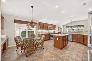 A spacious kitchen with a central island, wooden cabinets, and a dining area with wicker chairs. - Willie’s Place w/Golf Cart, Hot Tub & Dog Friendly (The Villages)