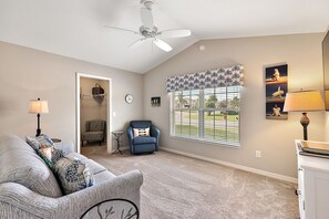 A living room with a ceiling fan, a blue armchair, a patterned sofa, a small table, and a window with blinds. - Willie’s Place w/Golf Cart, Hot Tub & Dog Friendly (The Villages)