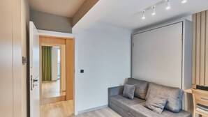 A modern living room with a grey sofa, wooden flooring, and a door leading to another room. - Apartamenty Swinoujscie -Matejki 1B (Swinoujscie)