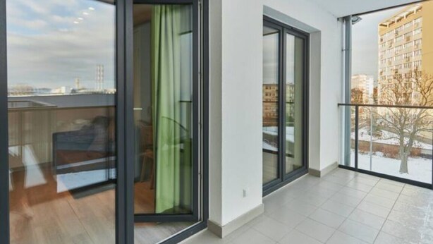 A modern apartment with large sliding glass doors, a balcony with a view of a cityscape, and a tiled floor. - Apartamenty Swinoujscie -Matejki 1B (Swinoujscie)