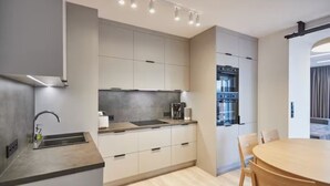 A modern kitchen with a built-in oven, a sink, and a dining area with a round table and chairs. - Apartamenty Swinoujscie -Matejki 1B (Swinoujscie)