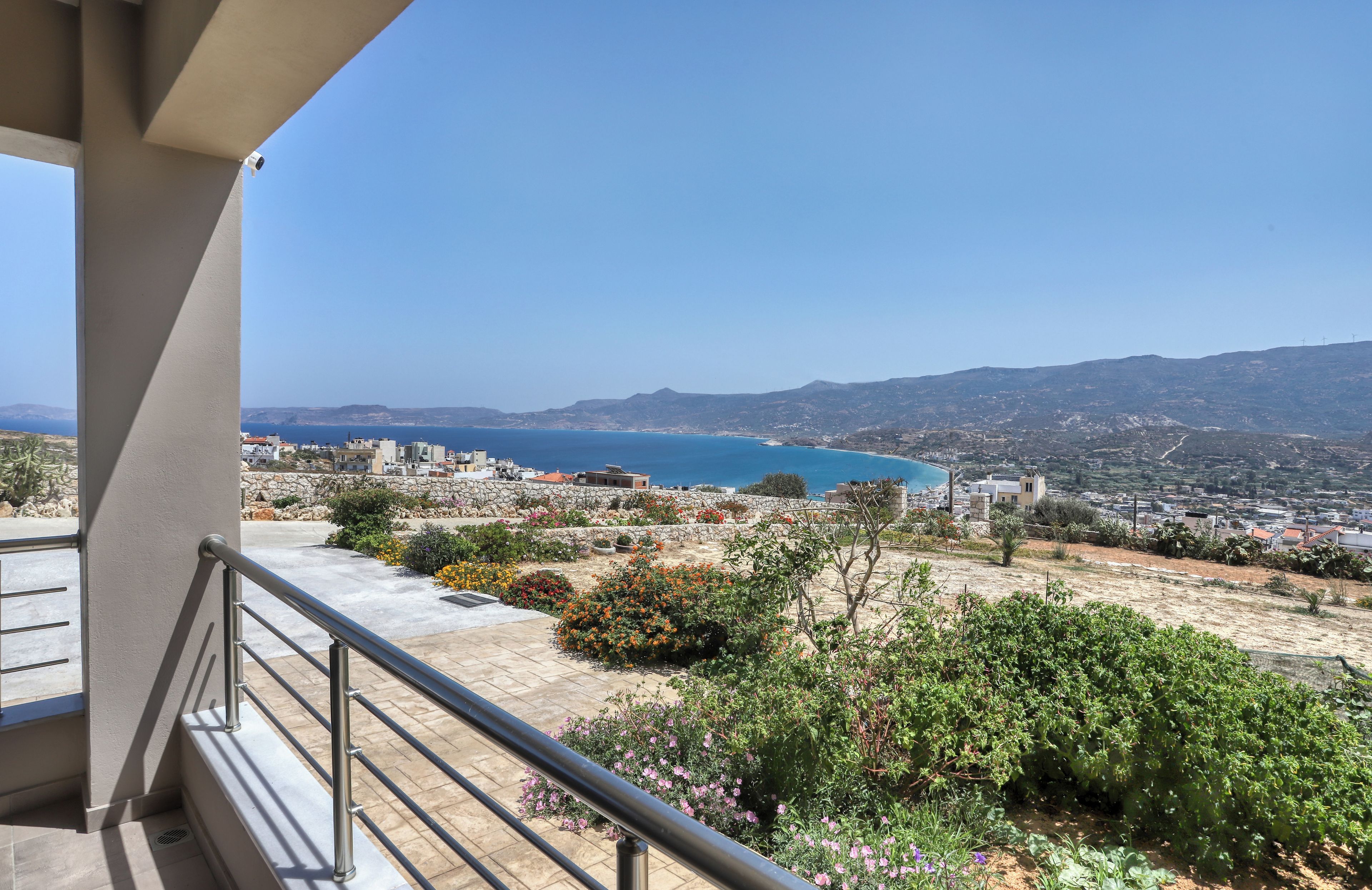A balcony with a view of a coastal town, a clear sky, and a distant mountain range.