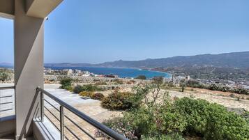 A balcony with a view of a coastal town, a clear sky, and a distant mountain range.