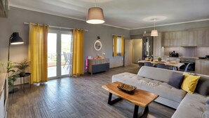 A spacious living area with a sofa, coffee table, and a dining table. There is a kitchen area with cabinets and a refrigerator. - Sitia Bay View Villa Apartment (Σητεία)