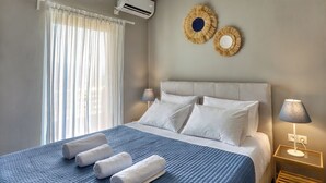 A hotel room with a bed, a bedside lamp, a wall-mounted air conditioner, and a window with sheer curtains. - Sitia Bay View Villa Apartment (Σητεία)