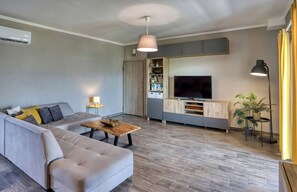 A modern living room with a sofa, coffee table, TV, and built-in entertainment unit. - Sitia Bay View Villa Apartment (Σητεία)