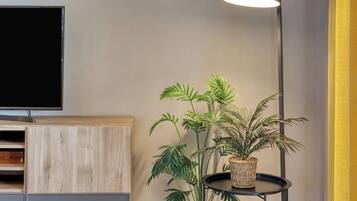 A modern living room with a flat-screen TV, a wooden cabinet, a floor lamp, and a potted plant.