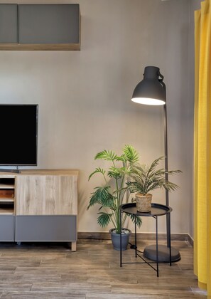 A modern living room with a flat-screen TV, a wooden cabinet, a floor lamp, and a potted plant. - Sitia Bay View Villa Apartment (Σητεία)