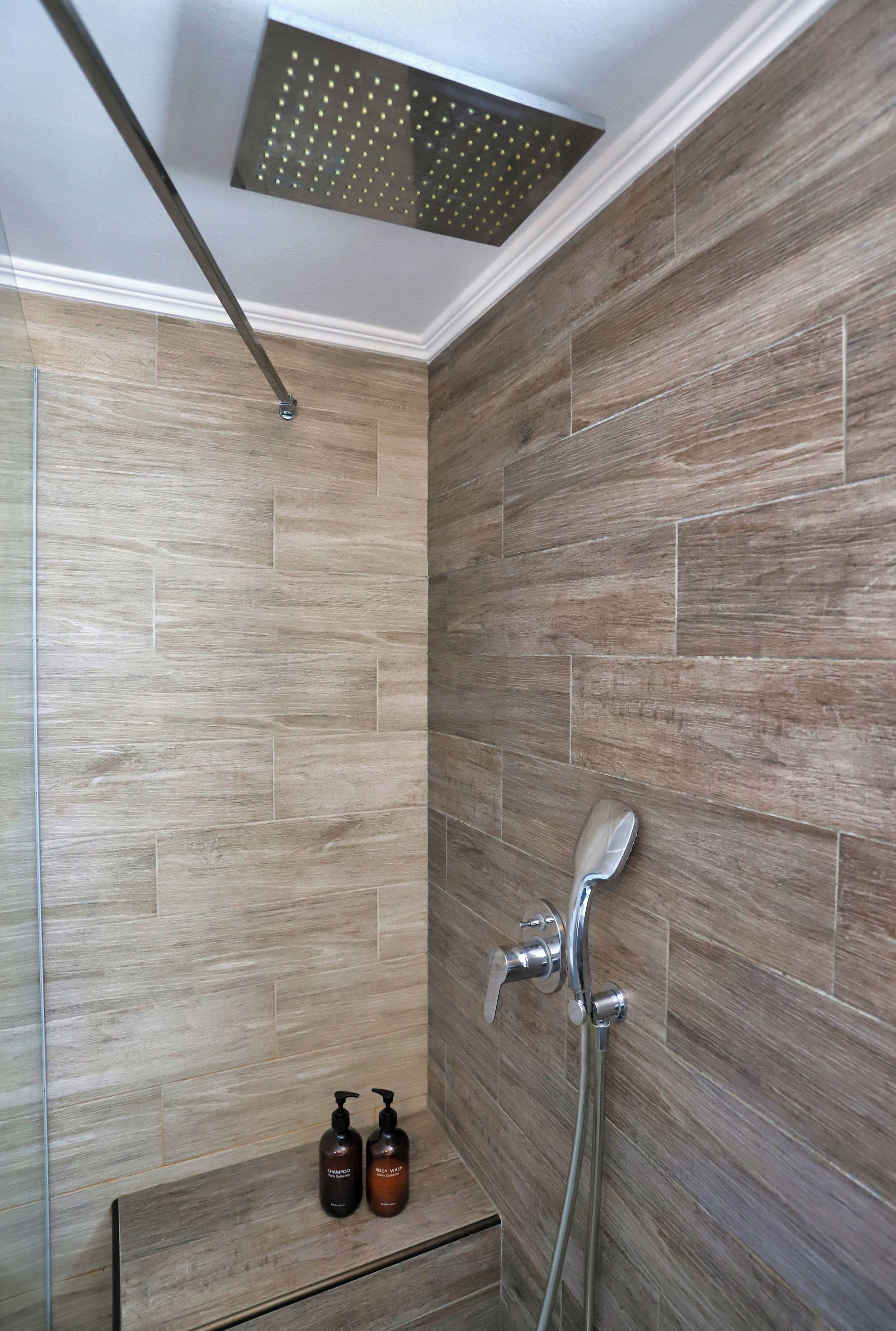 Dusche mit Regendusche, Handbrause und zwei Flaschen Shampoo und Duschgel auf einem Regal.