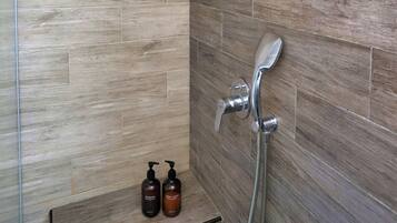 Dusche mit Regendusche, Handbrause und zwei Flaschen Shampoo und Duschgel auf einem Regal.
