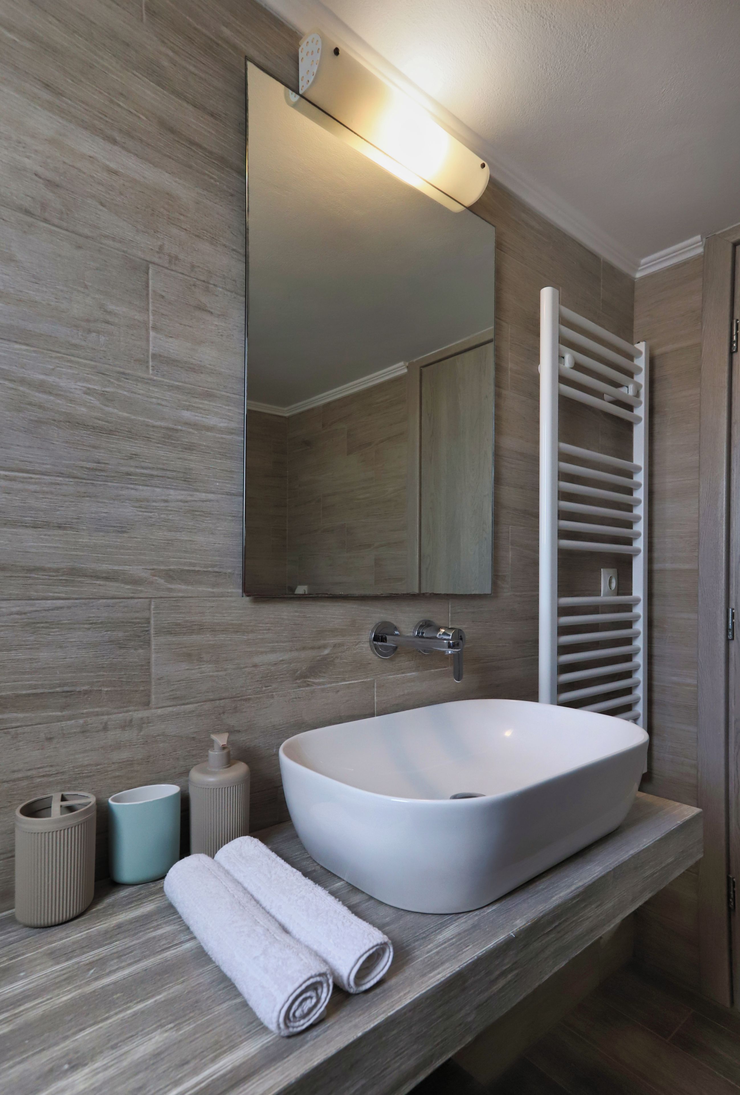 Une salle de bain comprenant un grand lavabo sur colonne, un miroir, un porte-serviettes et un porte-rouleau de papier toilette.