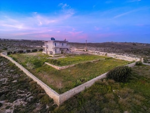 Une maison moderne à deux étages, dotée d’un mur en pierre qui entoure un espace verdoyant.