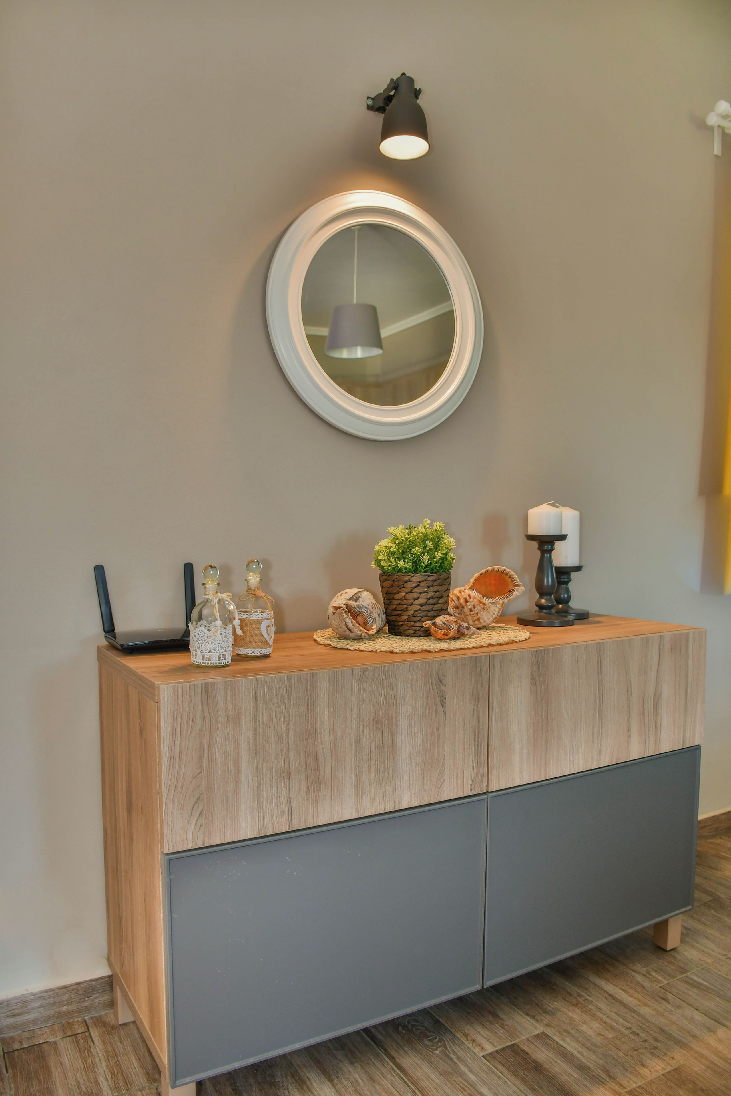 Una consola de madera con un espejo encima, una planta pequeña en maceta, conchas decorativas y un candelabro.