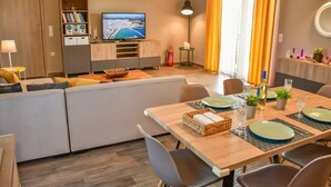En moderne stue med en sofa, spisebord dækket til fire personer, og et tv der viser et bybillede.