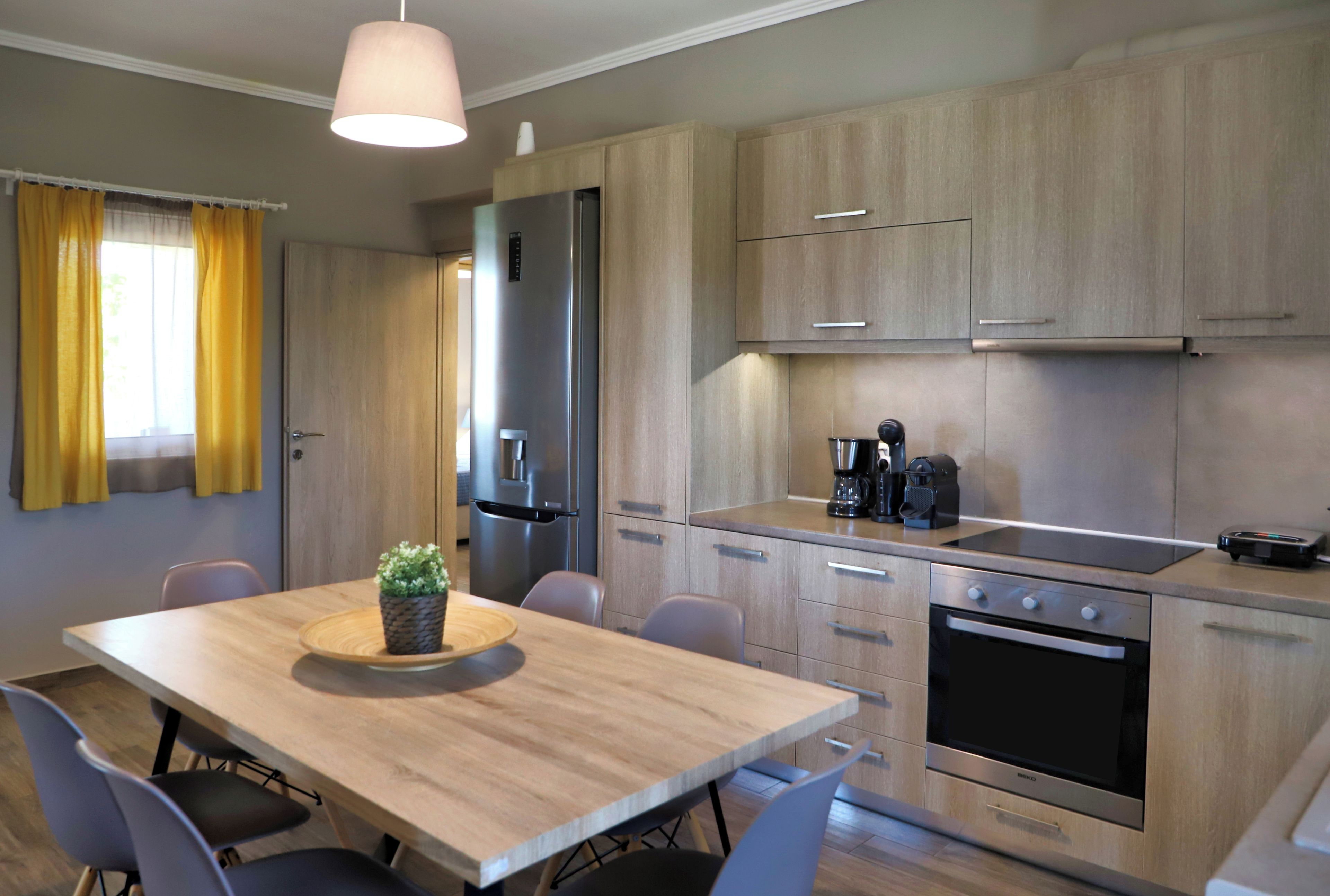 Een moderne keuken met houten kastjes, een inbouwoven en een eethoek met een tafel en stoelen.