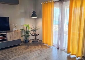 Un salon avec un téléviseur, une plante, une lampe et une fenêtre ornée de rideaux jaunes.