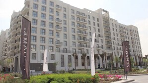 Un hotel de varios pisos con balcones, un jardín con flores y banderas con el nombre del hotel.