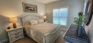 A bedroom with a bed, bedside tables, a lamp, a window with blinds, and a plant. - Coastal Retreat Minutes from the Beach/Oak Island and Historic Southport (Southport)