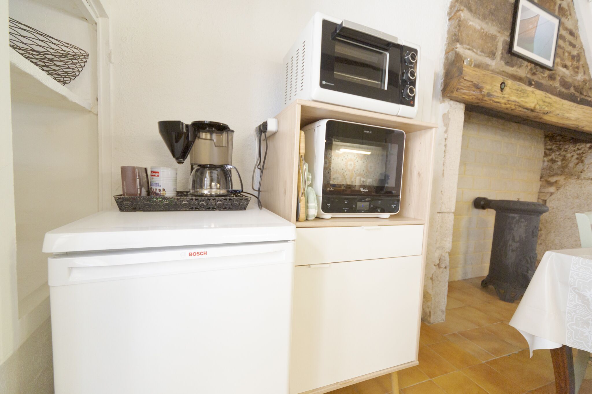 A compact kitchen with a Bosch refrigerator, a coffee maker, and a microwave on a wooden shelf.