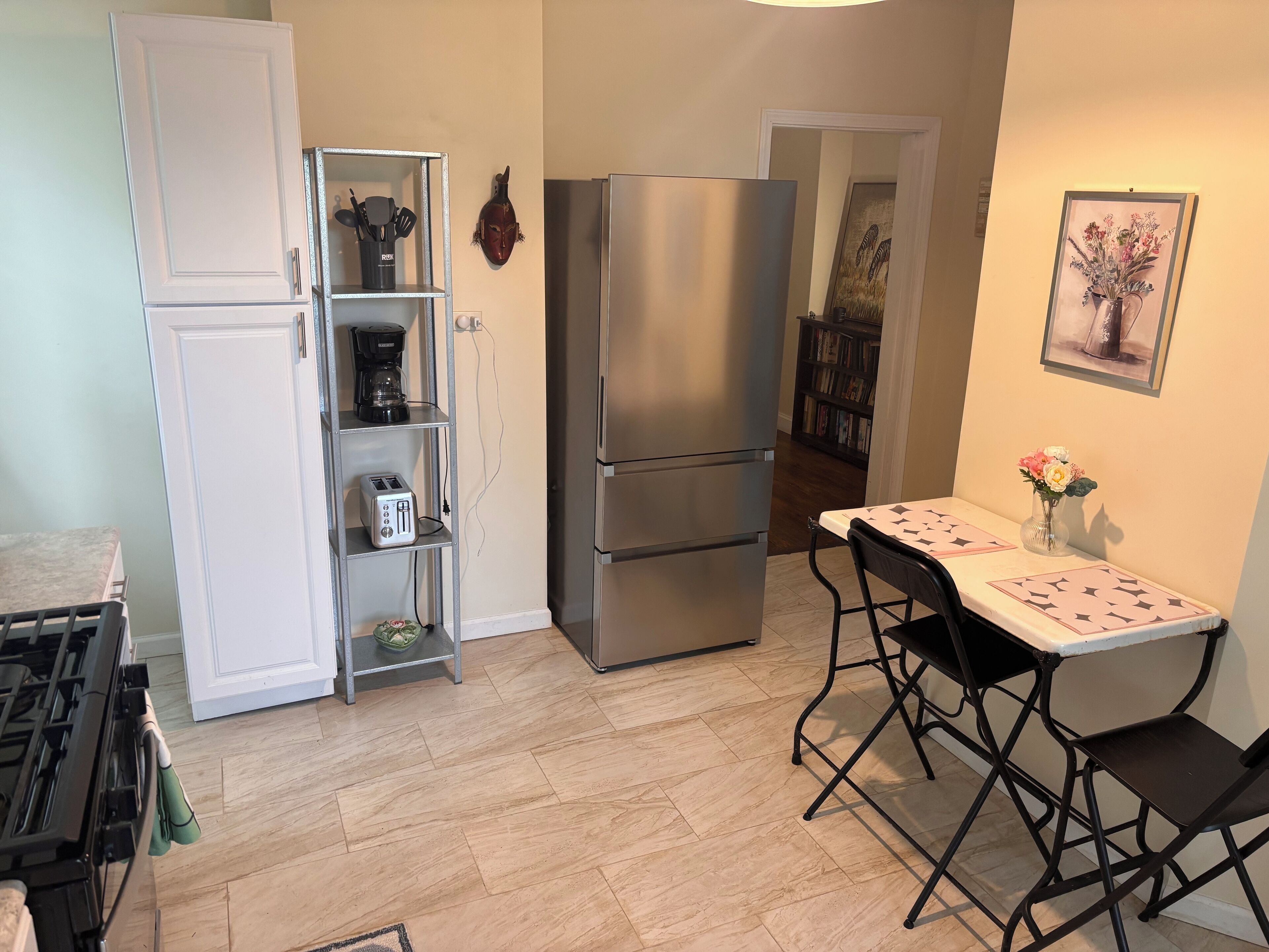 Cocina compacta con refrigerador de acero inoxidable, un mueble blanco con cafetera y un comedor con mesa y sillas.