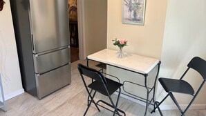 Cocina compacta con refrigerador de acero inoxidable, una pequeña mesa de comedor con dos sillas y un cuadro en la pared.