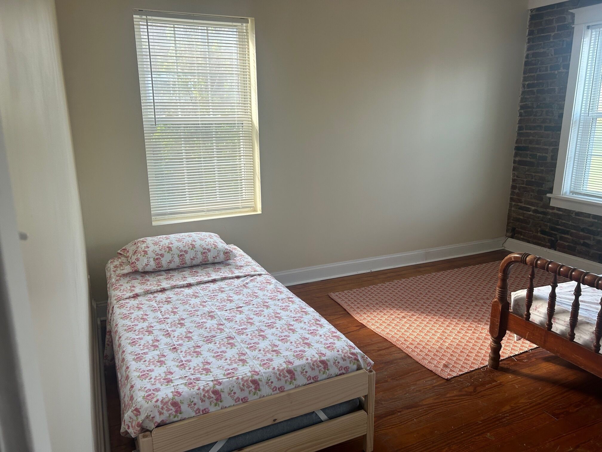 Um quarto pequeno e bem organizado, com uma cama de solteiro, uma cadeira de madeira e uma janela com persianas.