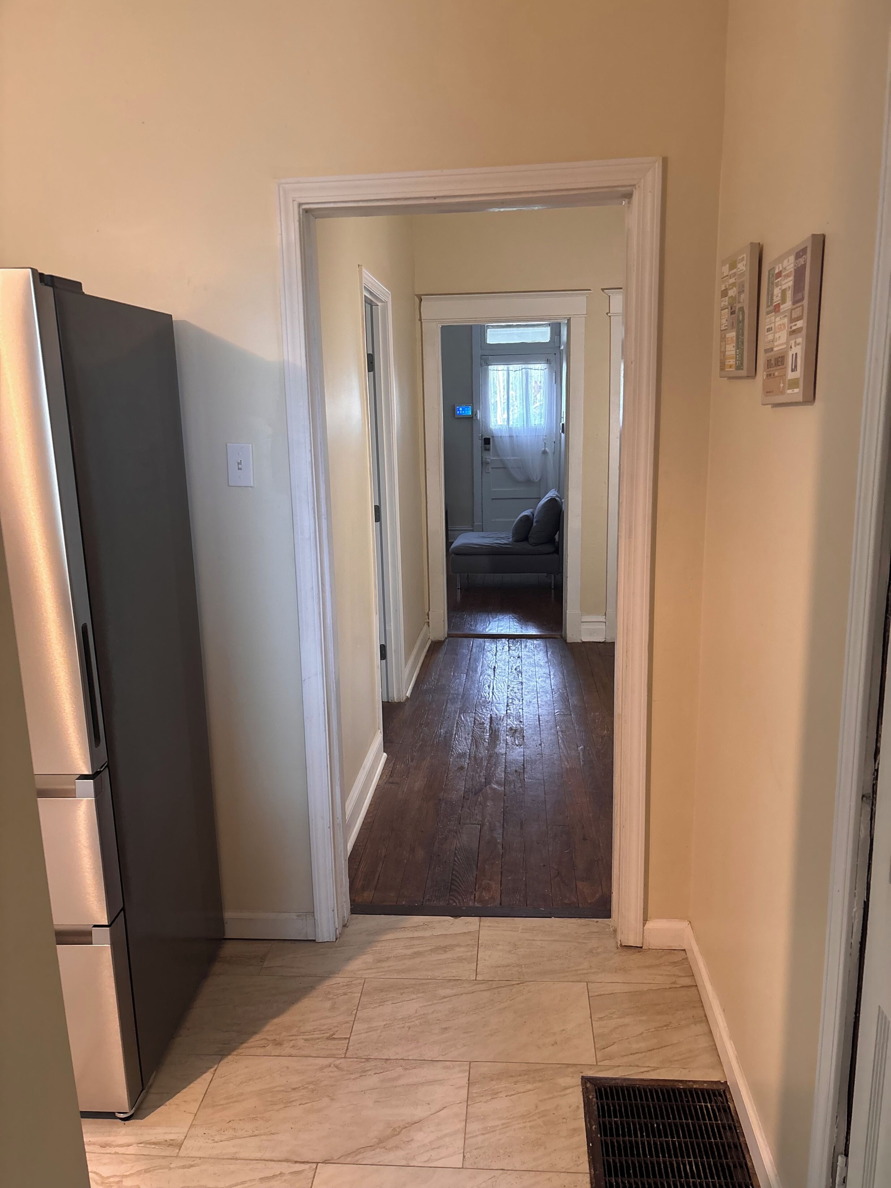 A hallway with a refrigerator on the left, a bench in the center, and a door leading to another room.